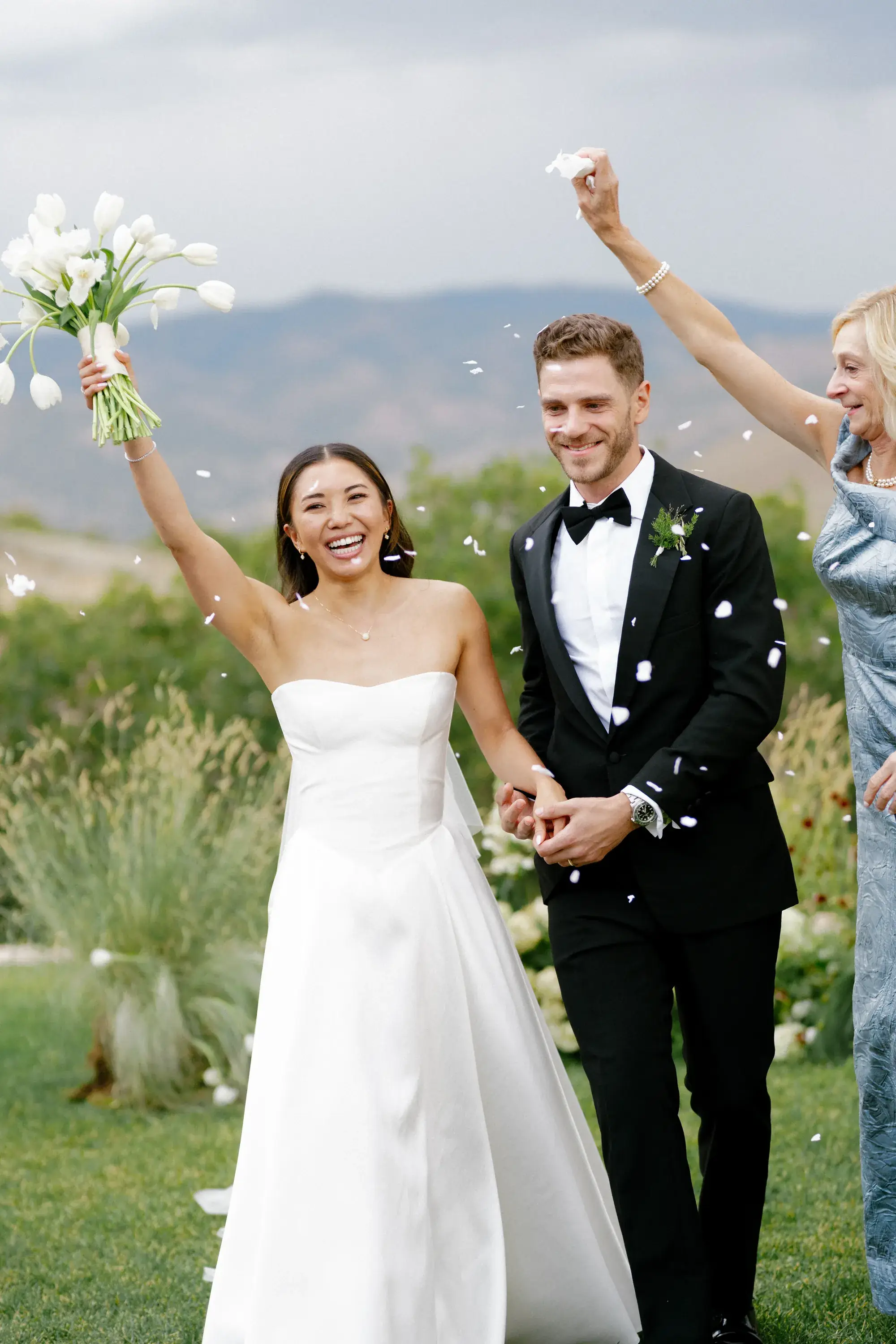 Bride raising her bouquet walking up the petal-covered aisle