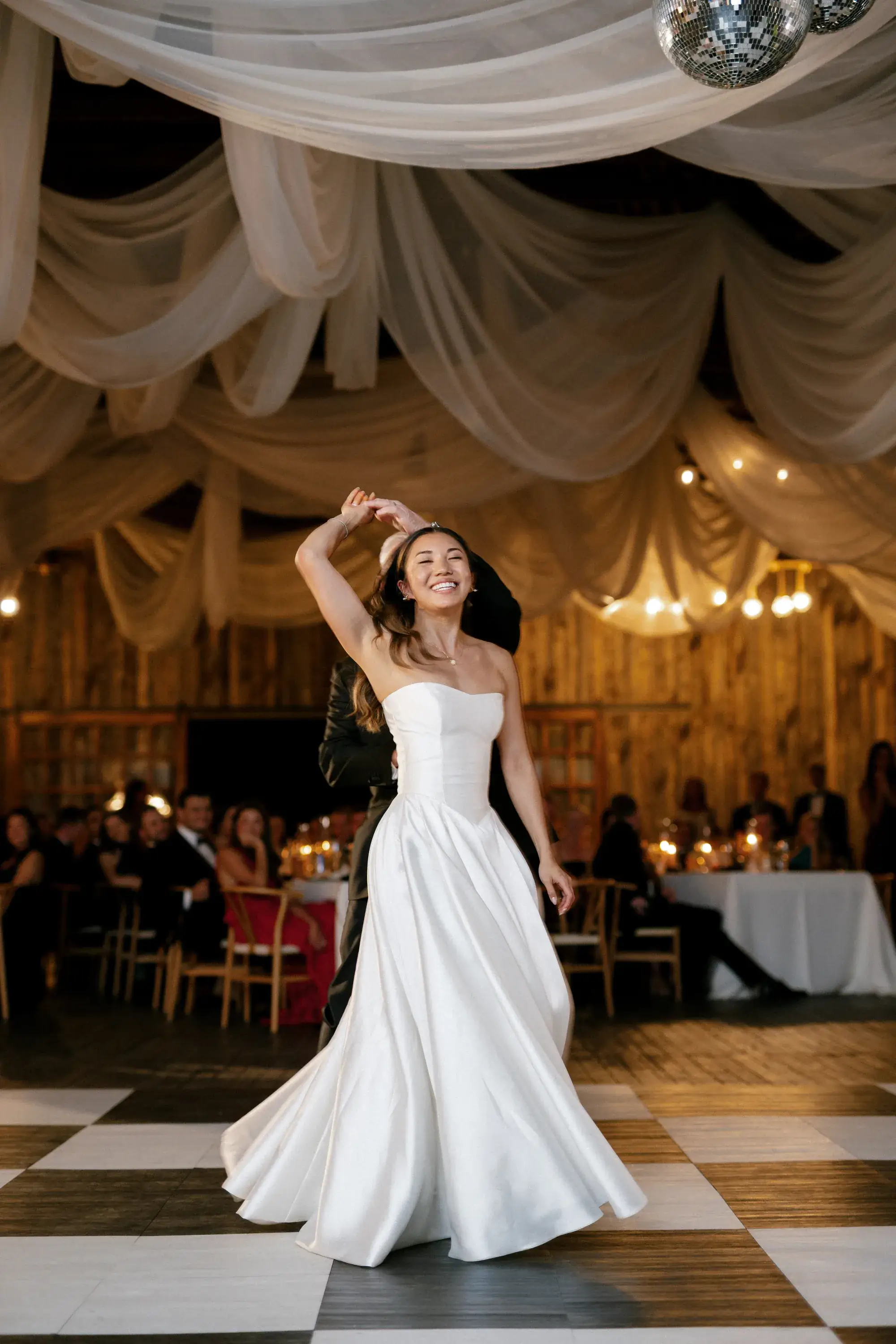 Bride twirling on a checkered dance floor beneath ivory drapes